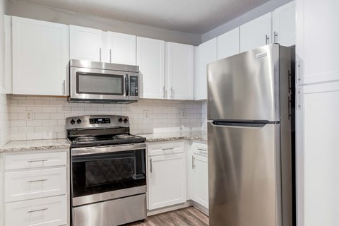 A kitchen with a stainless steel refrigerator, microwave, oven, and tiled backsplash.