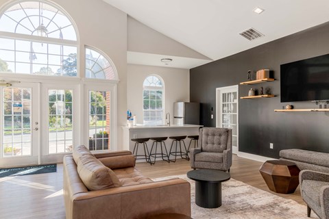 A living room in the clubhouse with a brown couch and a television on the wall.