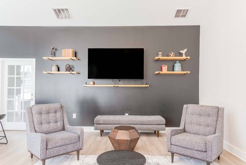 A living room in the clubhouse with a grey sofa, two chairs and a television.