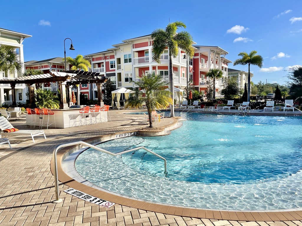 A pool surrounded by chairs and umbrellas with a building in the background.