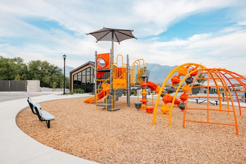 A playground with orange and black equipment and a brown bench.