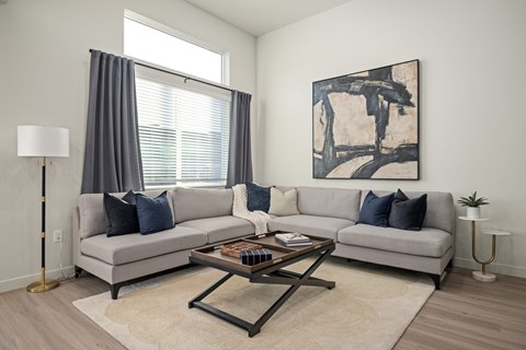 A living room with a grey couch, a coffee table, and a painting on the wall.