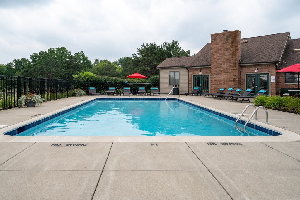 a swimming pool with lounge chairs and umbrellas in front of a brick building