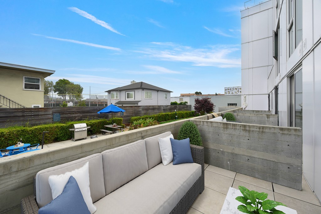 A modern outdoor seating area with a concrete wall and a grey couch.