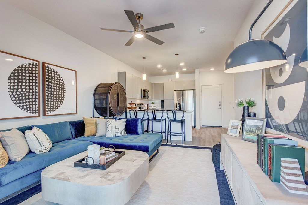 Model living room with ceiling fan and view of kitchen