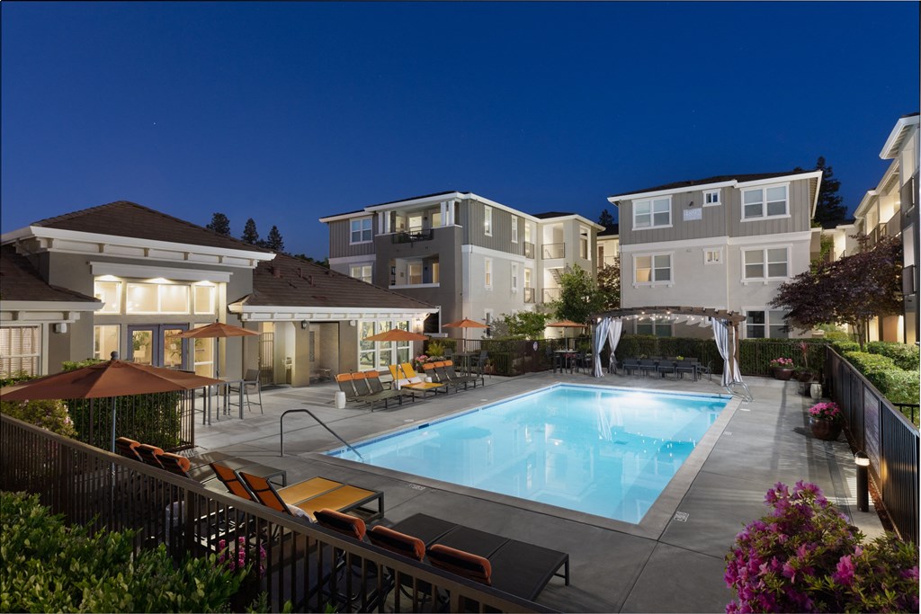 a swimming pool with lounge chairs and umbrellas in front of a building