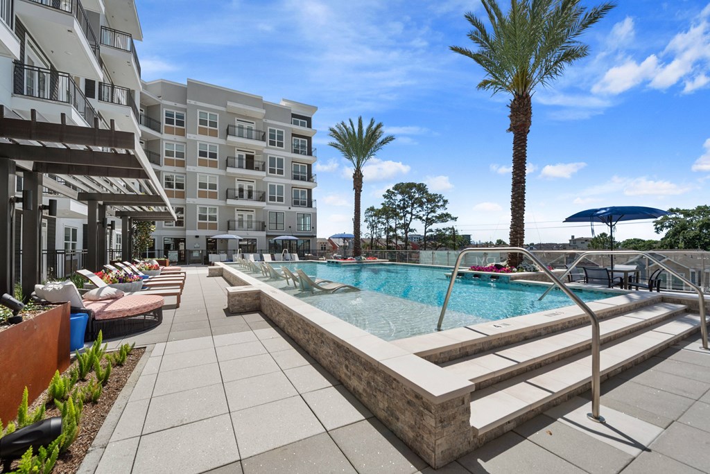 A swimming pool surrounded by a concrete patio and a building in the background.