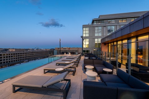 A rooftop pool area with lounge chairs and tables.