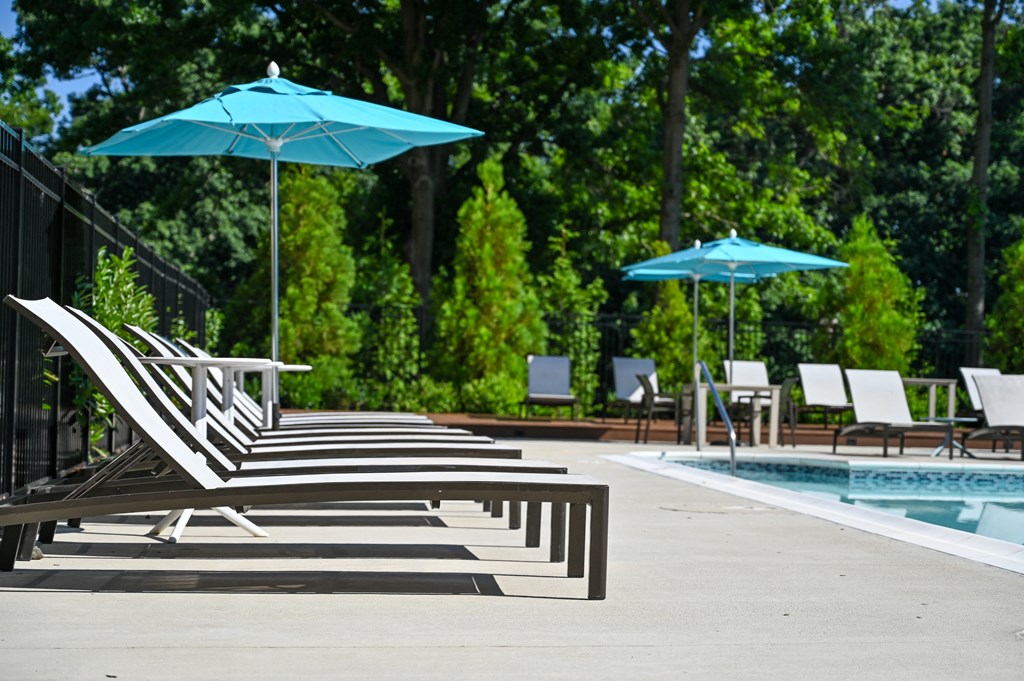 a poolside deck with chairs and umbrellas next to a pool