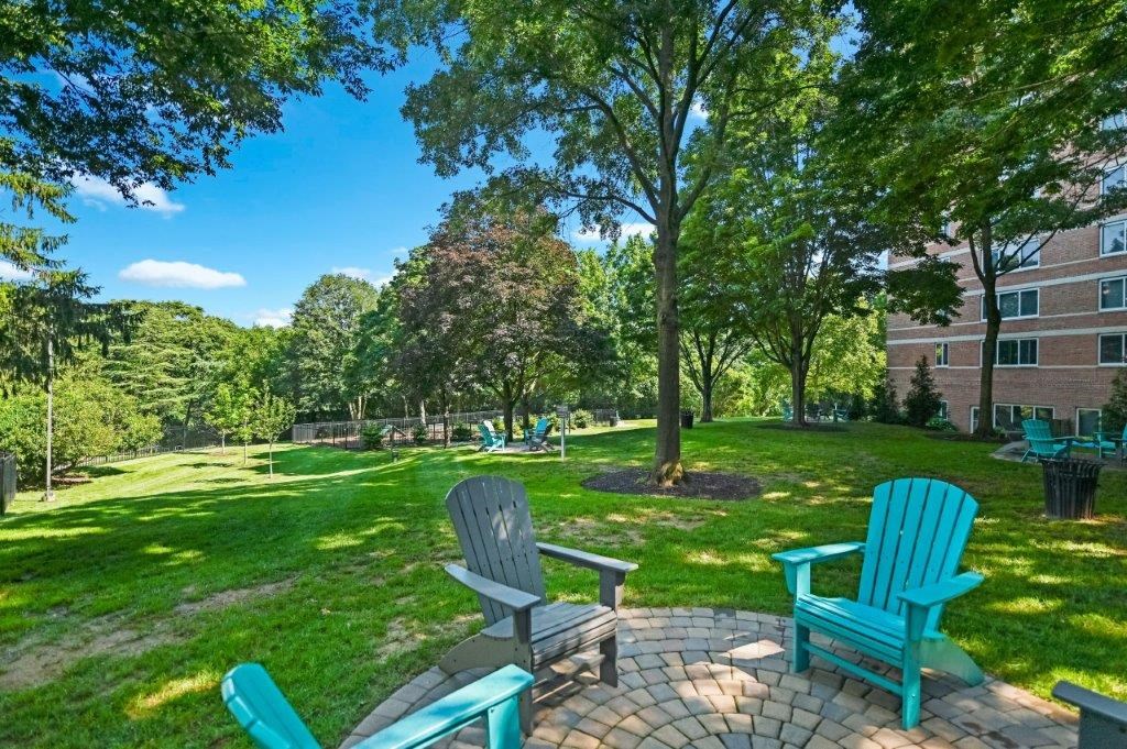 a backyard with green grass and blue chairs on a brick patio