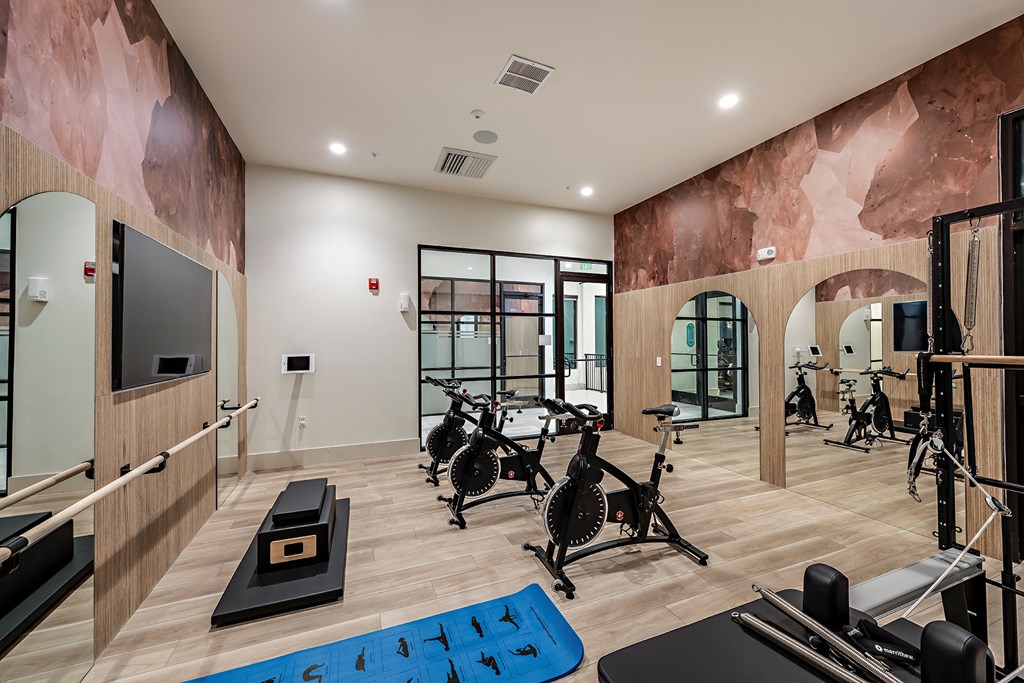 a gym with cardio machines and weights on a wooden floor and a large wall mural