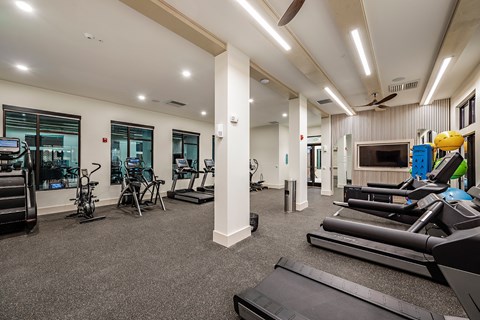 a gym with cardio equipment and weights in a building with windows