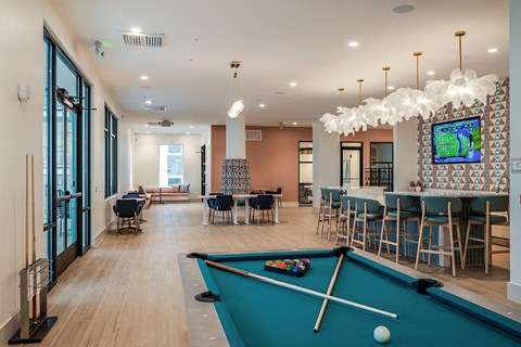a clubhouse with a pool table and a bar with tables and chairs
