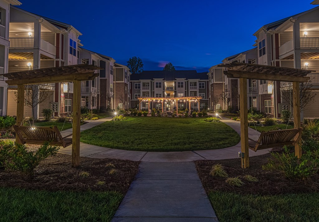 A well-lit walkway leads to a building with a grassy courtyard in the foreground.
