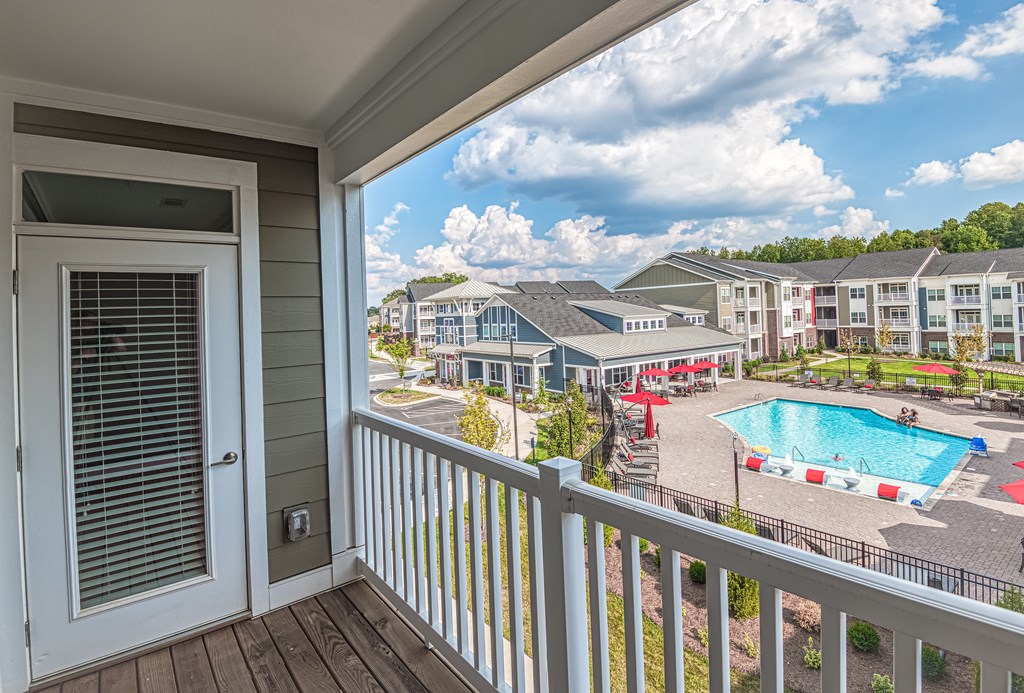 A balcony view of a pool area with a building in the background.
