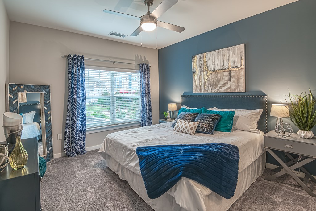 A bedroom with a bed covered in a blue blanket and a ceiling fan.