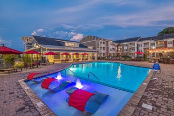 A swimming pool with red and blue loungers and a building in the background.