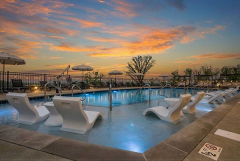 A pool with white chairs and a sunset in the background.