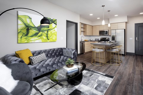 A modern living room with a grey couch and a green abstract painting on the wall.