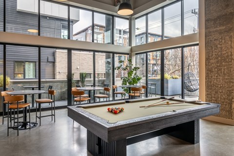 A pool table is in the middle of a room with a view of the outside.