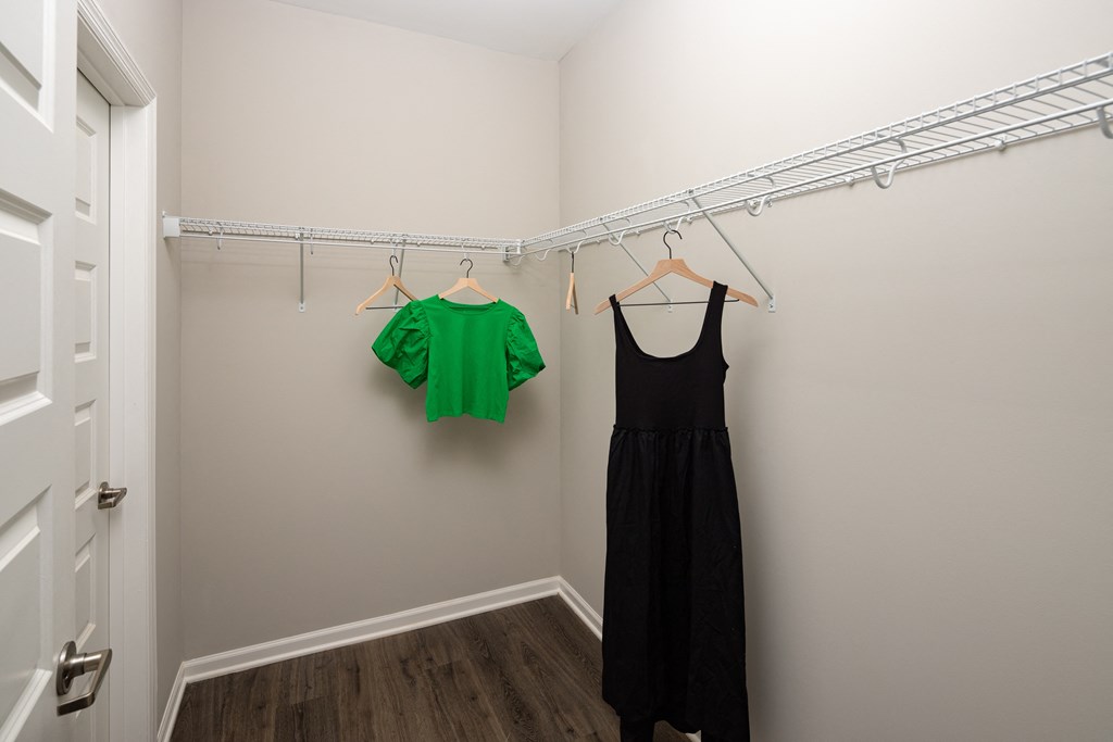 a walk in closet with a black dress and a green shirt hanging on a white rod