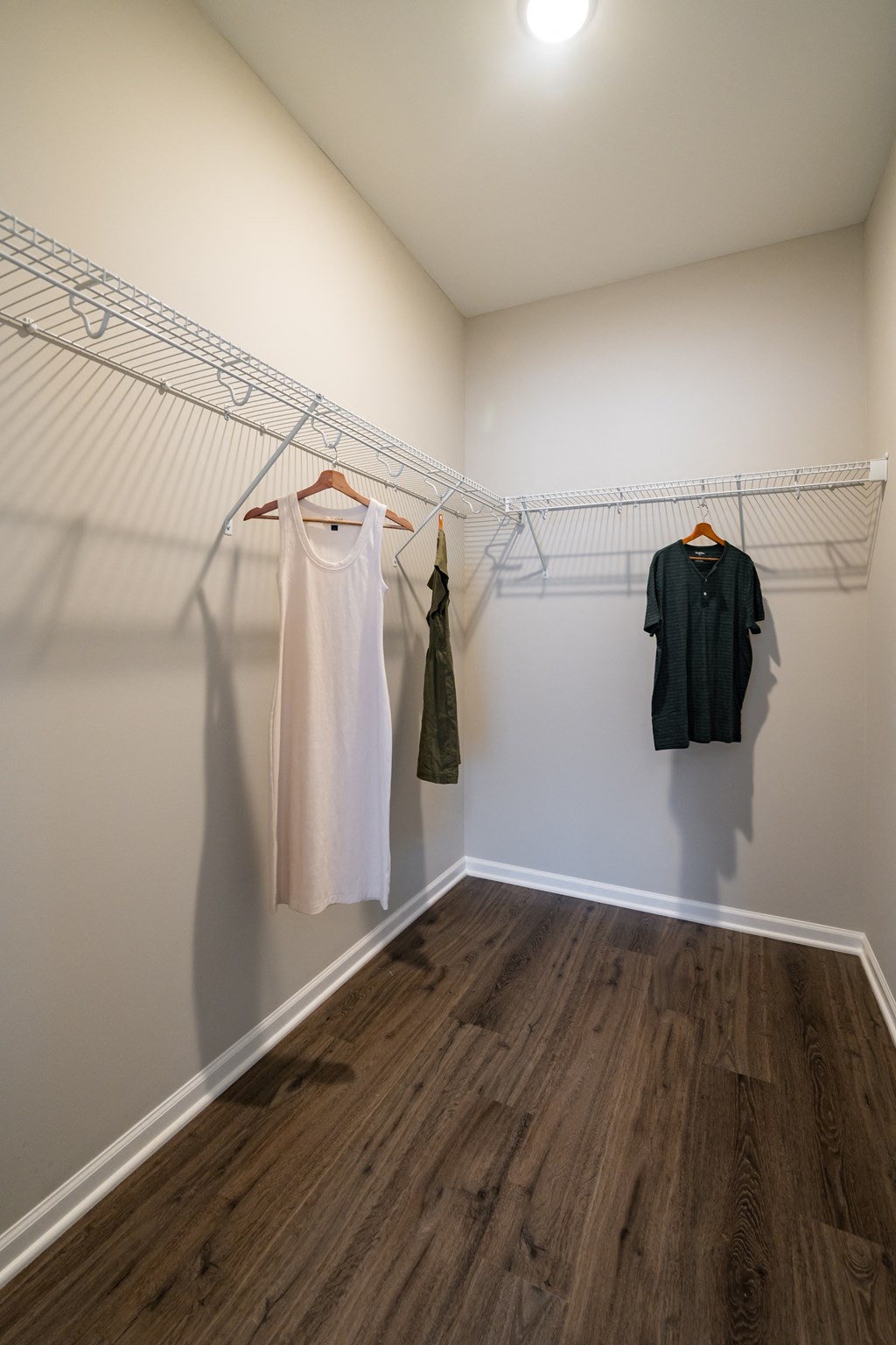 a walk in closet with white walls and wood floors