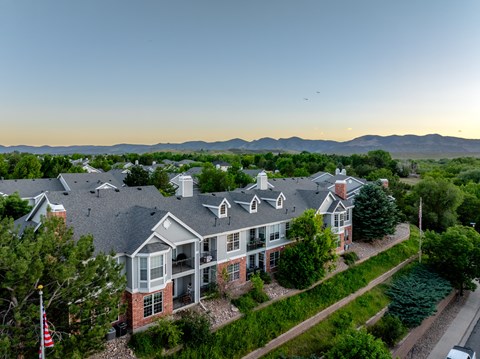 A large house with a flag on the left side is surrounded by greenery and has a mountain range in the background.