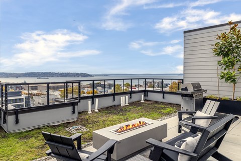 A patio with a fire pit and chairs overlooking a cityscape.