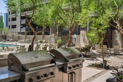 A grill is in the middle of a patio with trees and chairs around it.