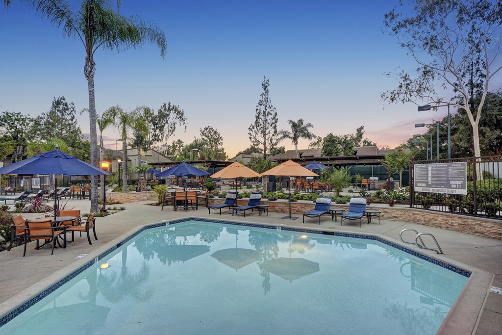 A large swimming pool surrounded by blue umbrellas and wooden benches.