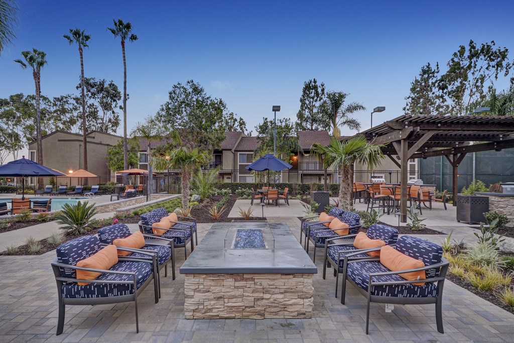A patio with a fire pit surrounded by chairs and tables.