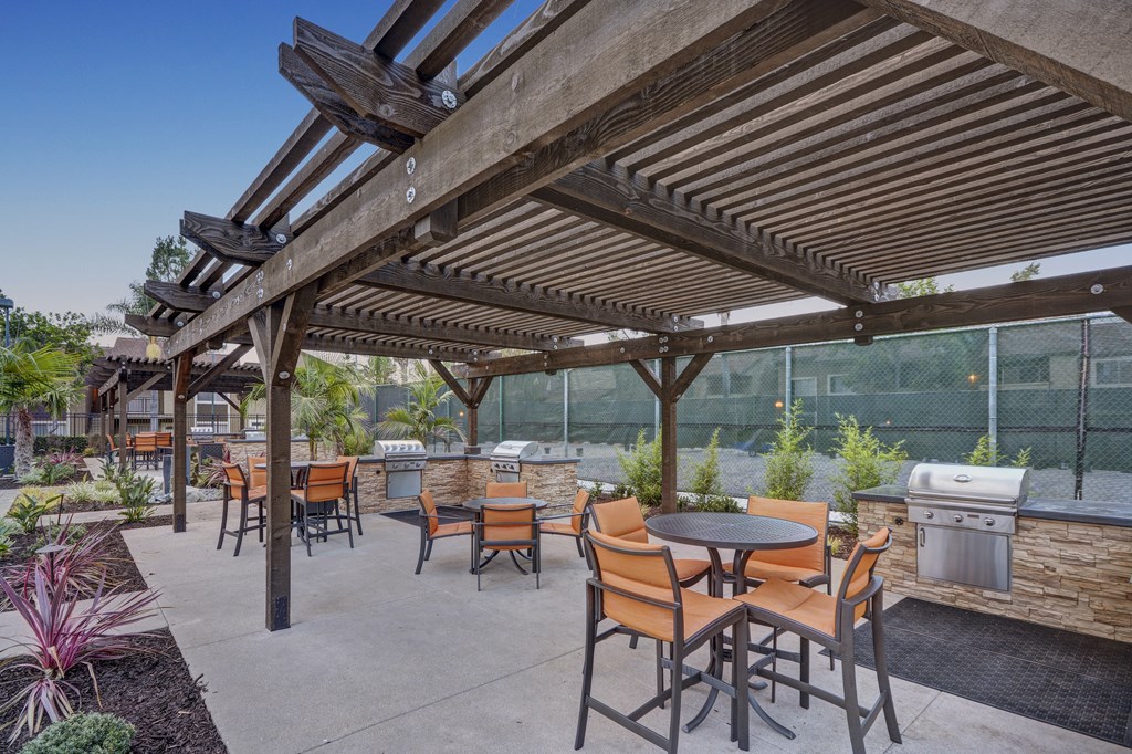 A patio with tables and chairs under a wooden pergola.