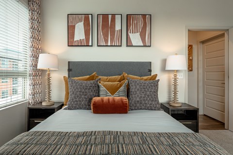 A bedroom with a bed, two lamps, and three framed artworks on the wall.