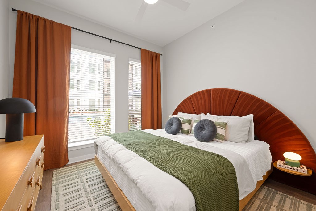 A bedroom with a large bed and a window with orange curtains.