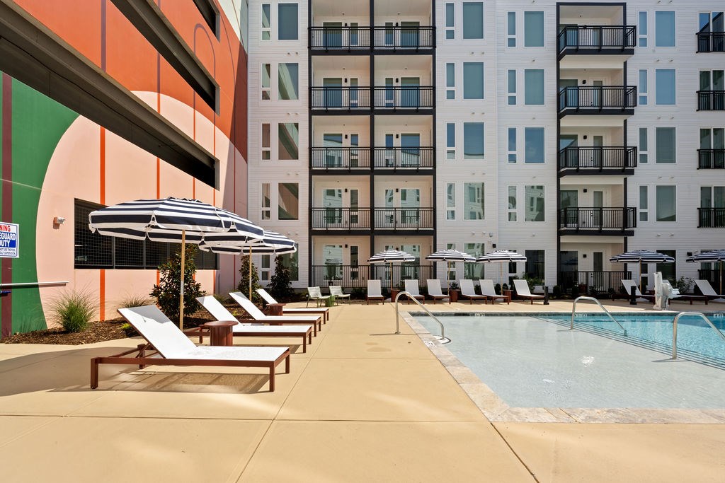 A pool area with sun loungers and umbrellas in front of a building.
