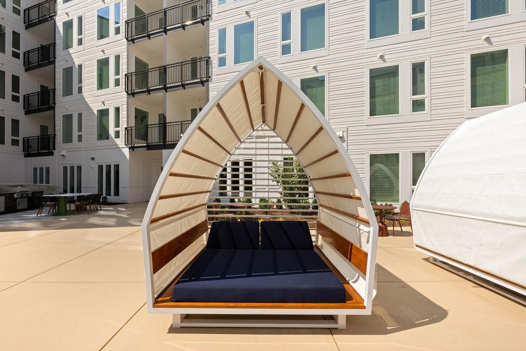A white boat-shaped lounge chair with a blue cushion is in front of a building.