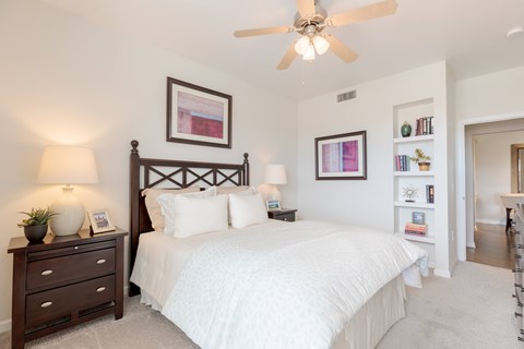 A bedroom with a large bed, a ceiling fan, and a nightstand with a lamp.