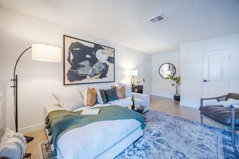 A living space with a white sectional sofa, carpet, and lamps in an apartment at Sage at Green Valley.