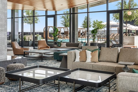 Interior club room with a glass coffee table and couches large window facing the exterior pool