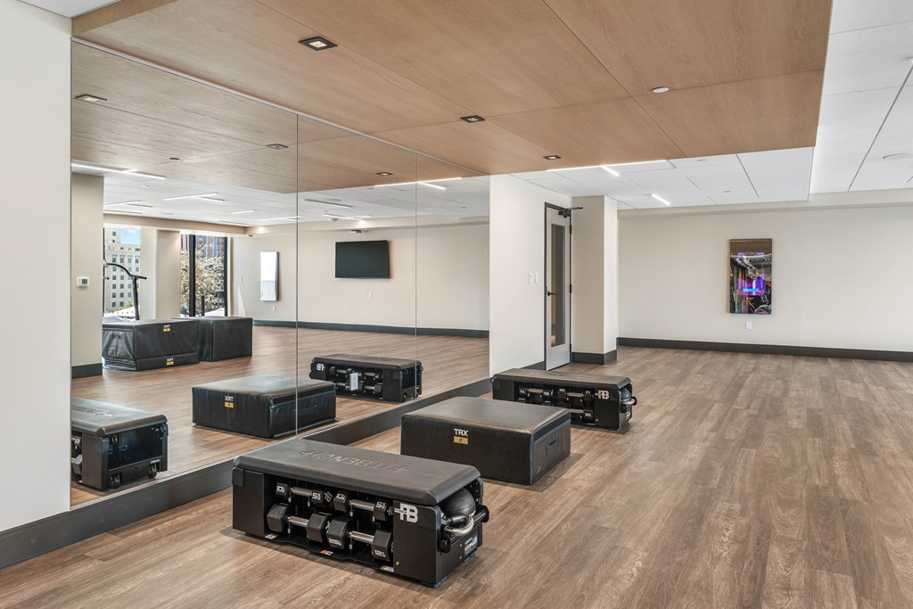 Fitness room with black boxes on the floor and a TV mounted on the wall large mirrors