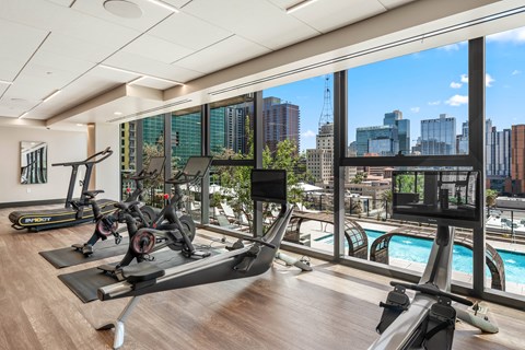 Interior gym with treadmills, exercise bikes, and a television with a view of the city.