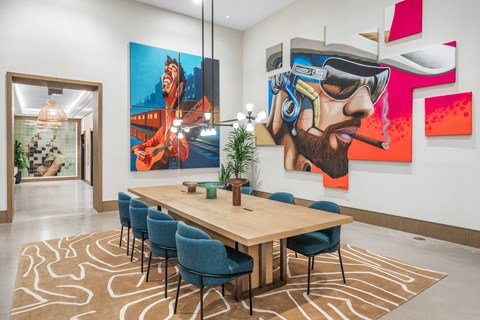 A conference room with a long table and chairs, a carpet on the floor, and two paintings on the wall.