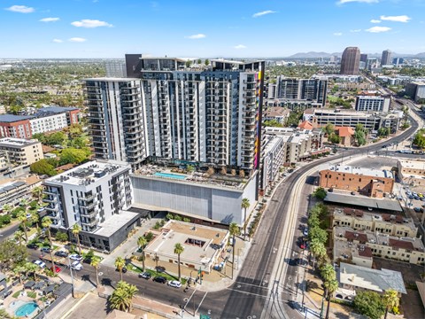 Exterior building with a pool on the roof is surrounded by other buildings and palm trees.