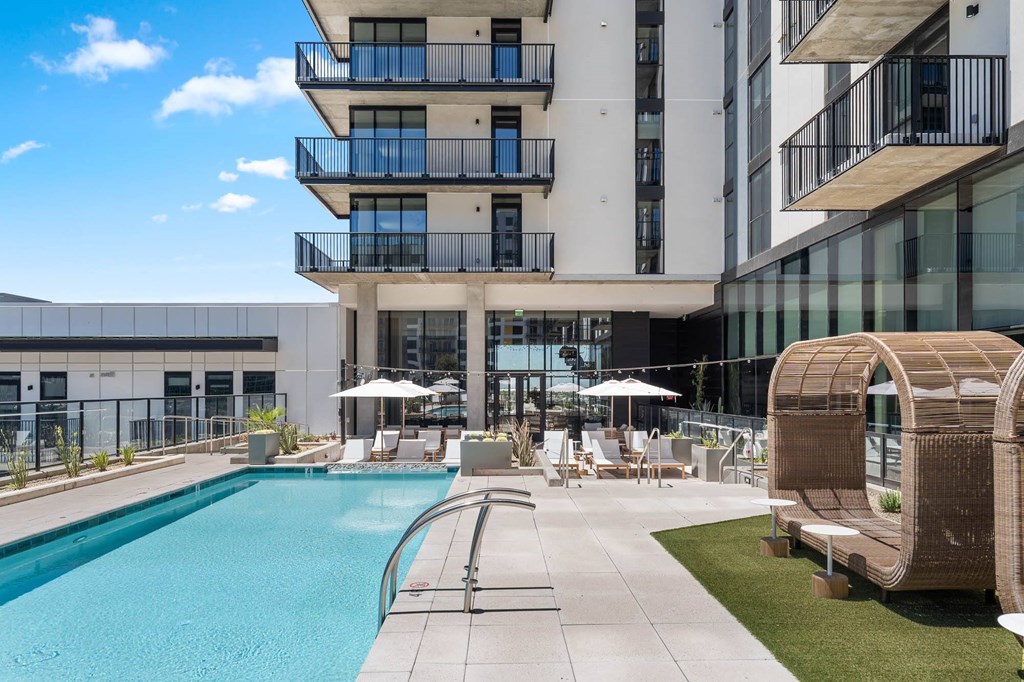 A modern building with a pool and lounge chairs.