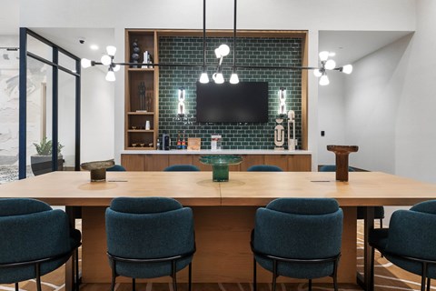 Interior club house area with mounted tv, long table with chairs, light fixtures.