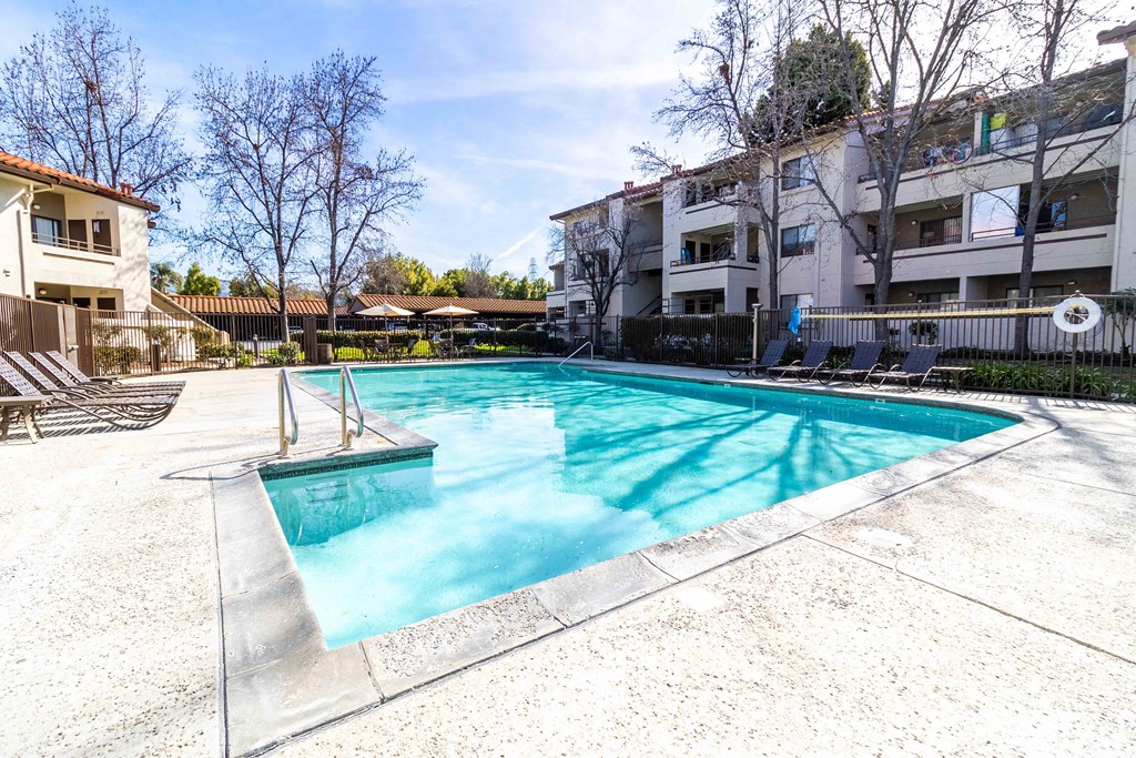 A swimming pool surrounded by a concrete floor and a metal fence.