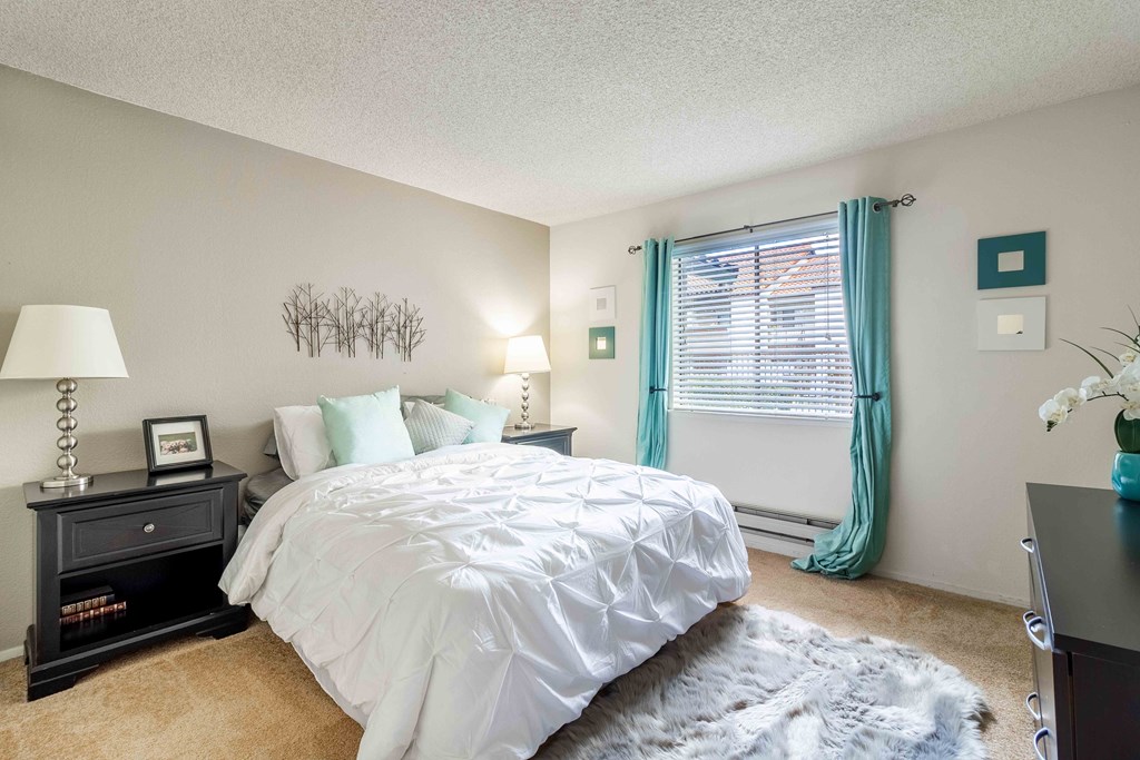 A bedroom with a white bed and a black nightstand.