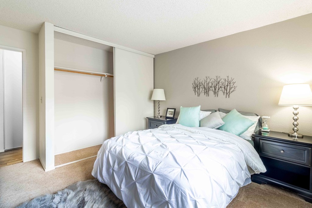 A bedroom with a large bed, a nightstand with a lamp, and a wall art.