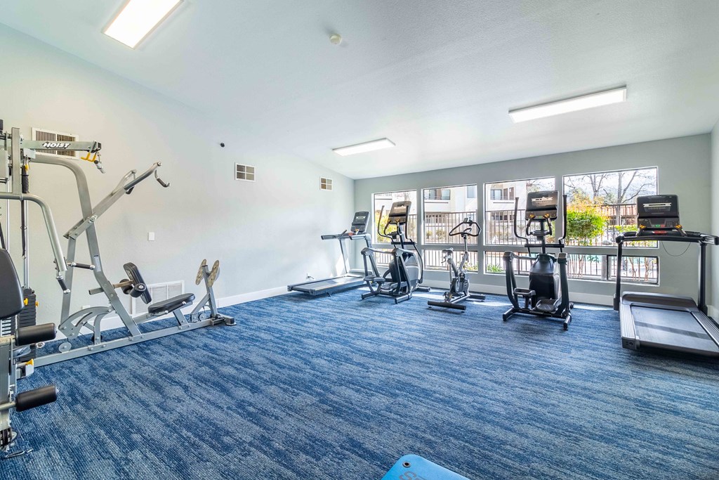 A spacious gym with a variety of equipment including a treadmill, elliptical machines, and a weight bench.