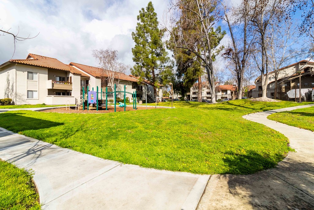 A sunny day at a park with a playground and apartment buildings in the background.